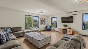 A modern living room with a sectional sofa, a coffee table, a TV, and large windows.