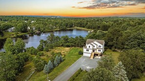 A two-story house with a front porch, surrounded by a lake and dense forest.