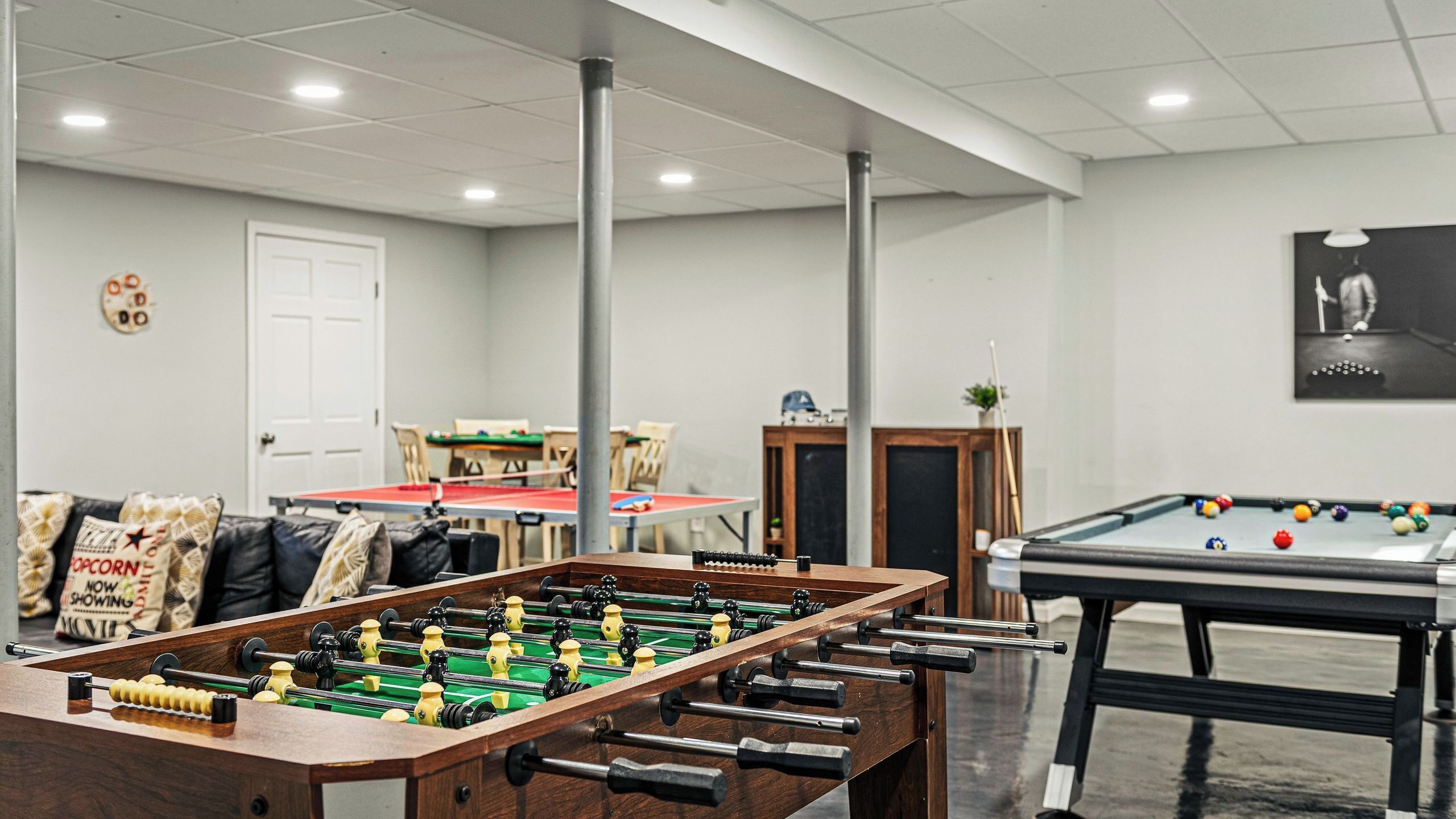 A room with a foosball table, a pool table, and a billiards table.