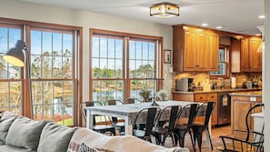 A spacious kitchen with large windows, wooden cabinets, and a dining area with a table and chairs. - Laker's Pointe by Avantstay Lakefront Private Peninsula Hot Tub, Game Room (Long Pond)