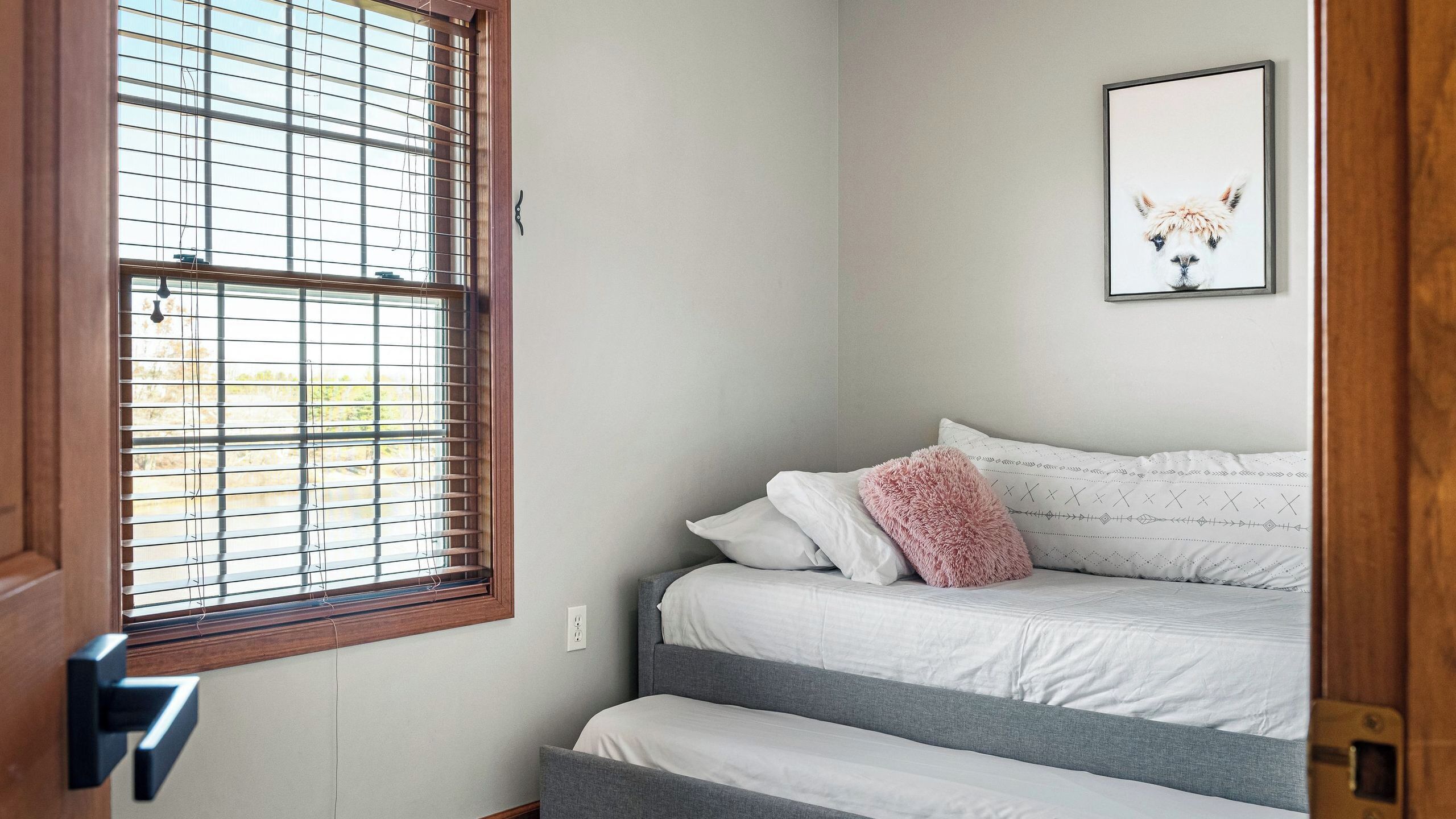 Une chambre à coucher avec un lit, une fenêtre avec des stores, une porte et un tableau encadré au mur.