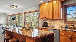 A kitchen with wooden cabinets, a granite countertop, and a large window. - Laker's Pointe by Avantstay Lakefront Private Peninsula Hot Tub, Game Room (Long Pond)