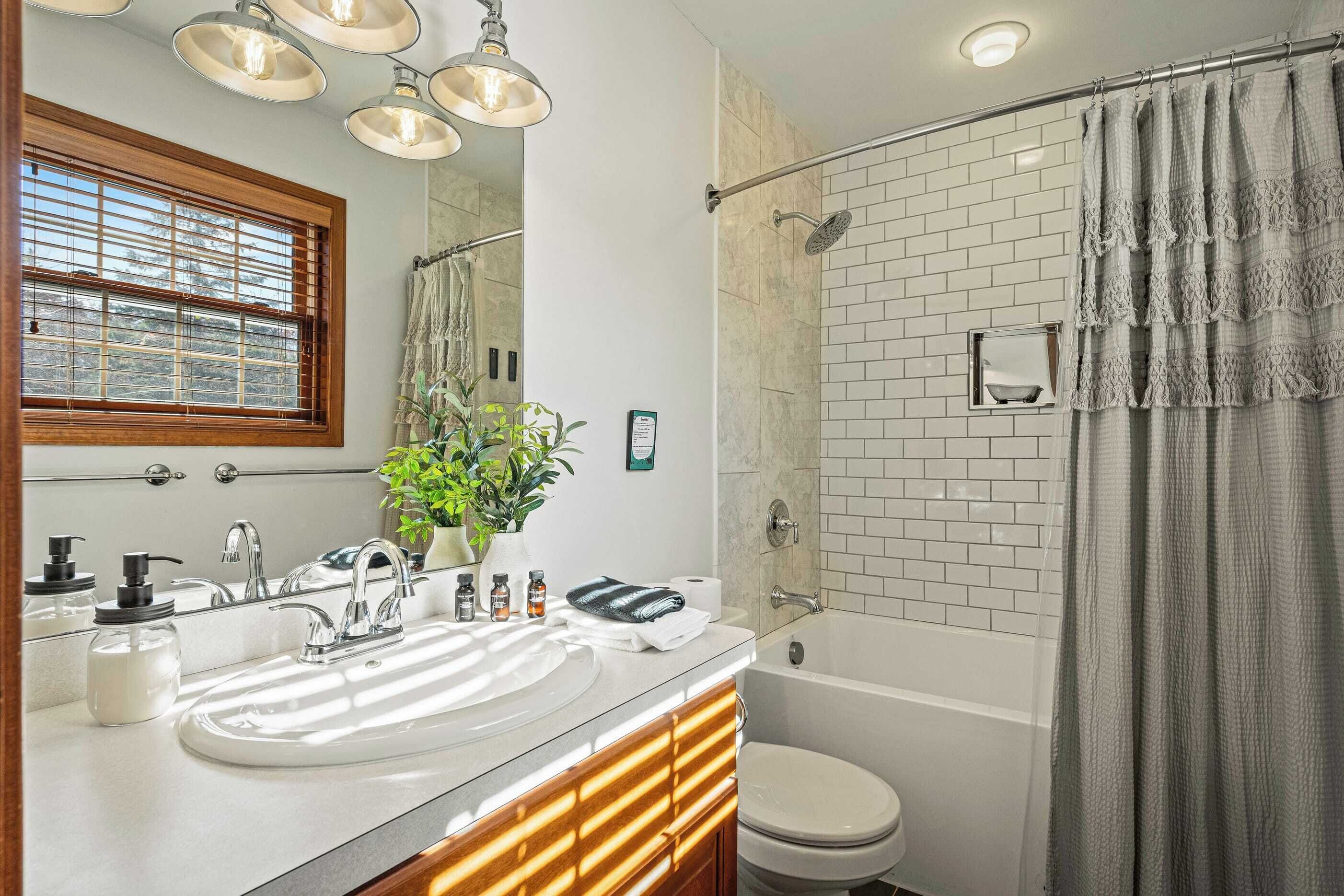 A modern bathroom with a large mirror, a white sink, a shower, and a toilet.