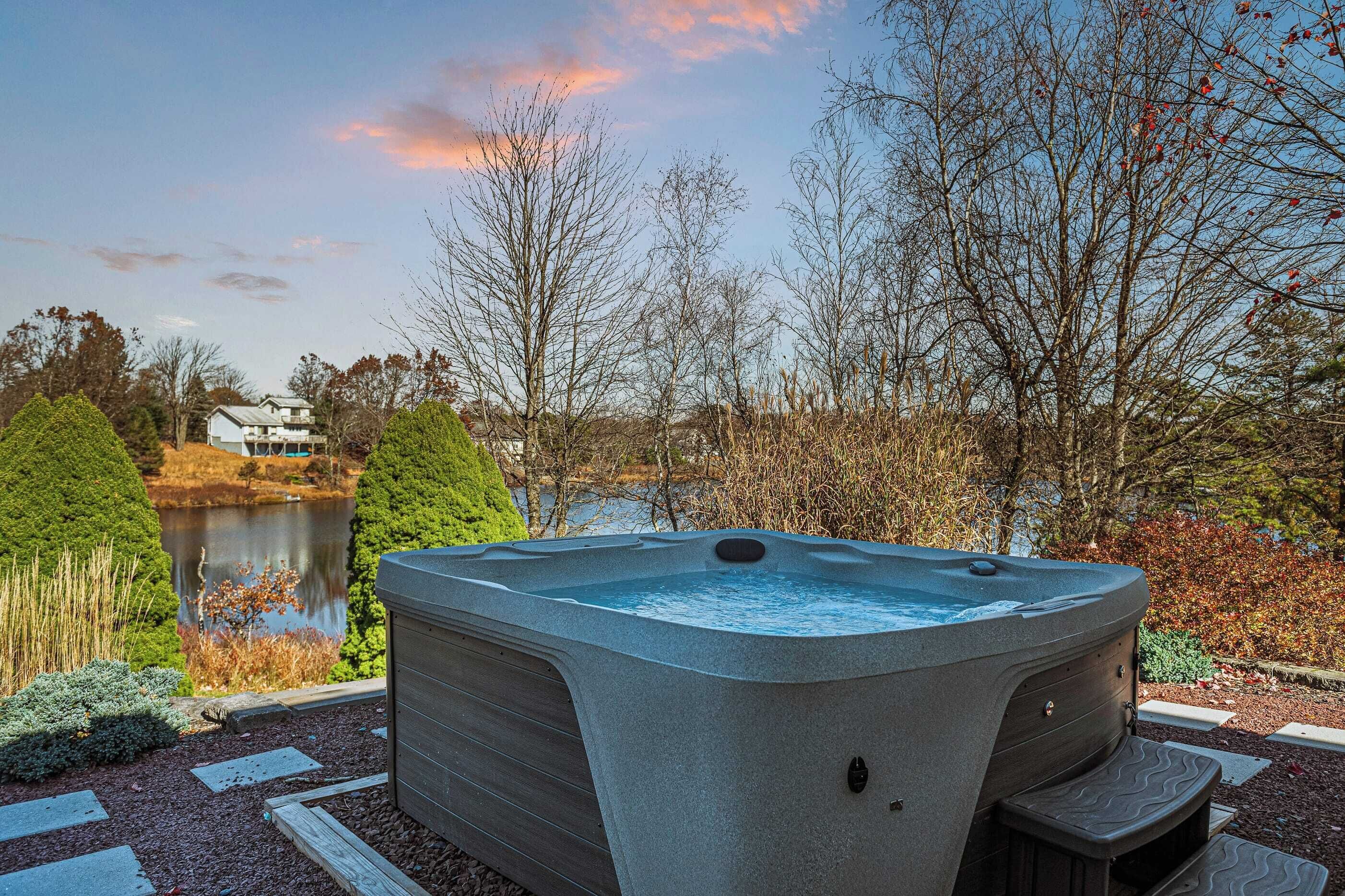 Un bain à remous aménagé dans un espace paysager, avec un lac et des arbres en arrière-plan.