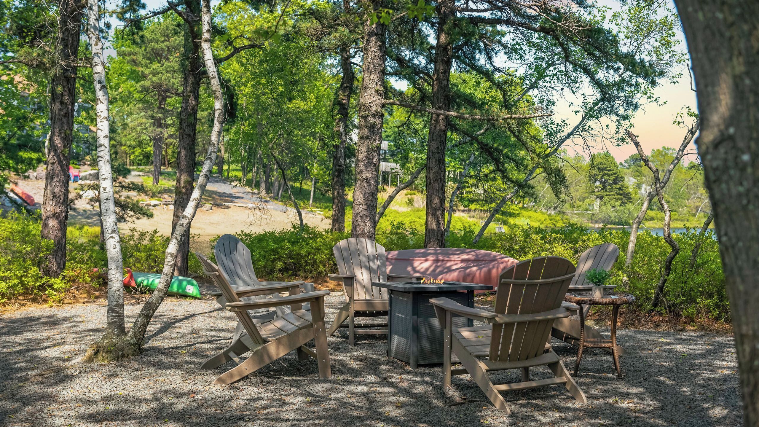 Un espace extérieur aménagé avec une table et des chaises, entouré d’arbres et offrant une vue sur un lac.