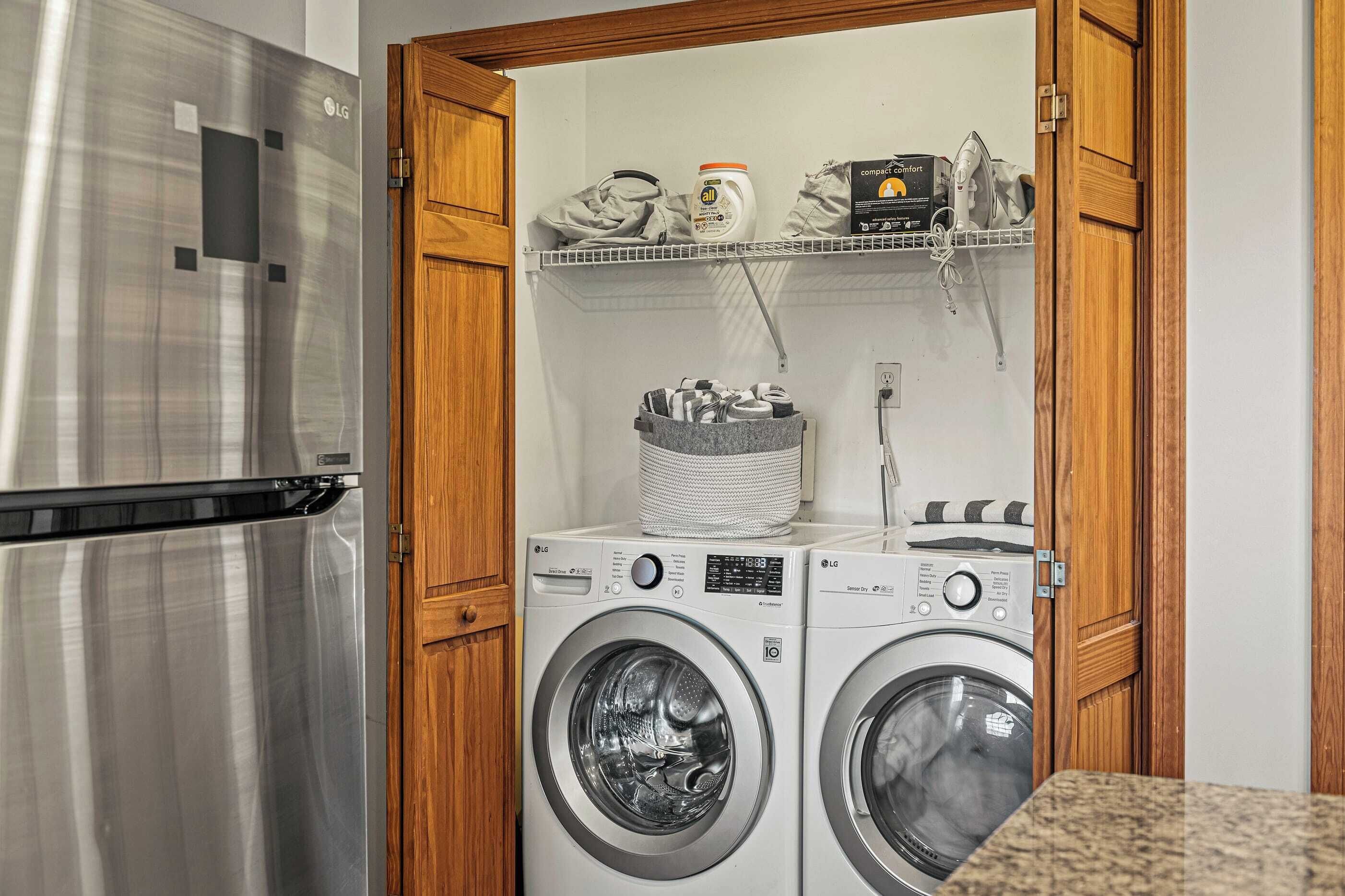 Un área de lavandería con dos lavadoras de carga frontal, un refrigerador de acero inoxidable y un estante con productos de limpieza.