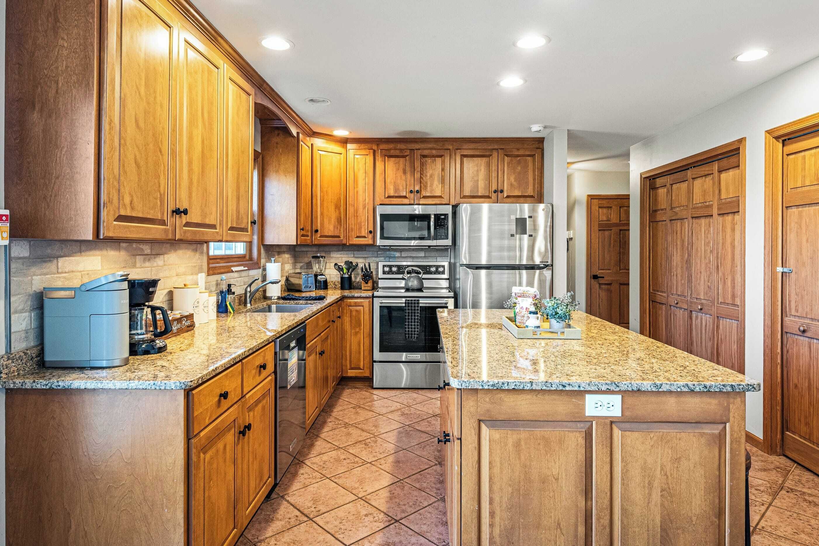 A kitchen with wooden cabinets, stainless steel appliances, granite countertops, and a tiled floor.