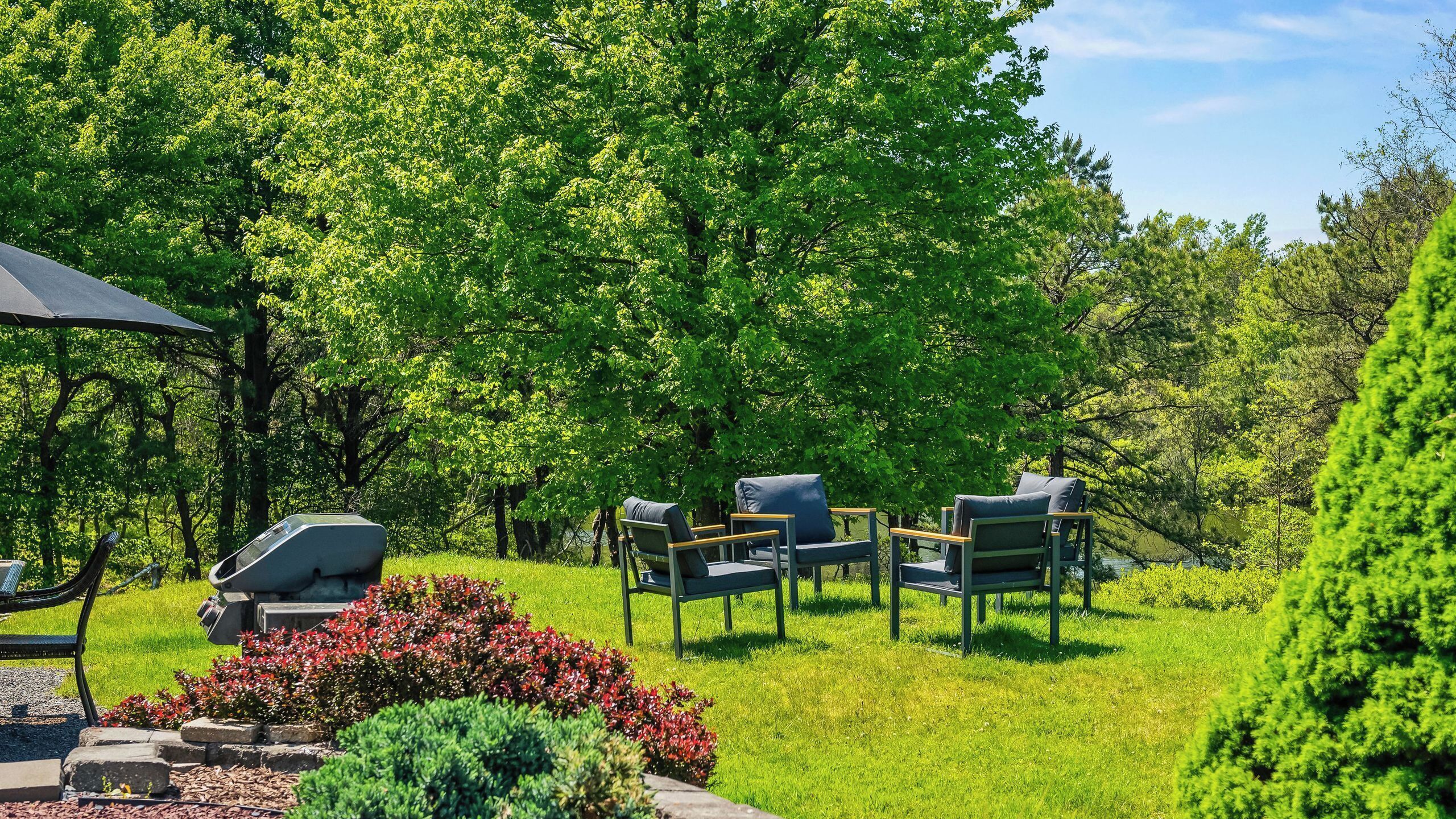 A grassy outdoor area with a barbecue grill, two lounge chairs, and a table.
