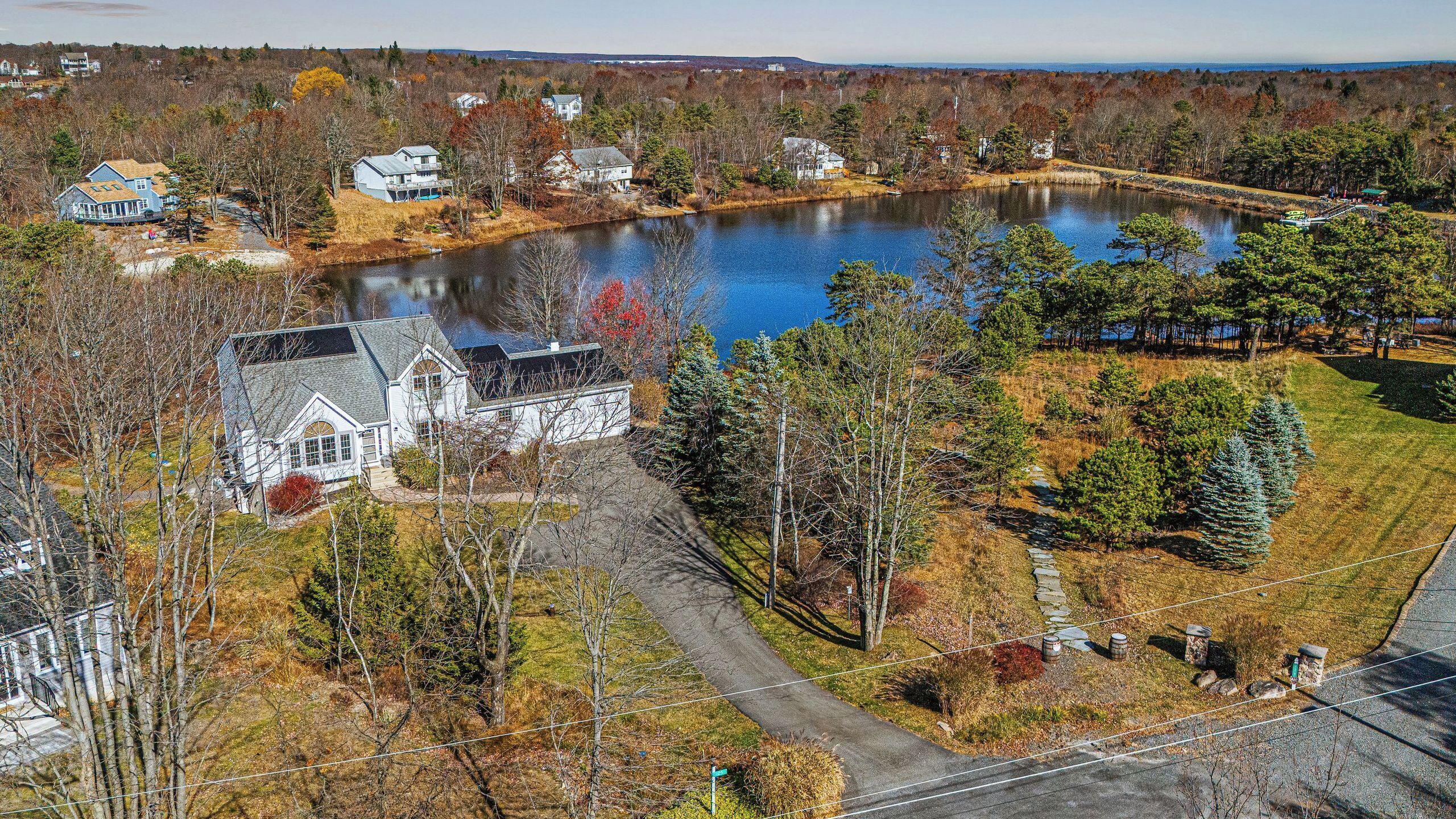 A large house with a pond, surrounded by trees and a clear sky.