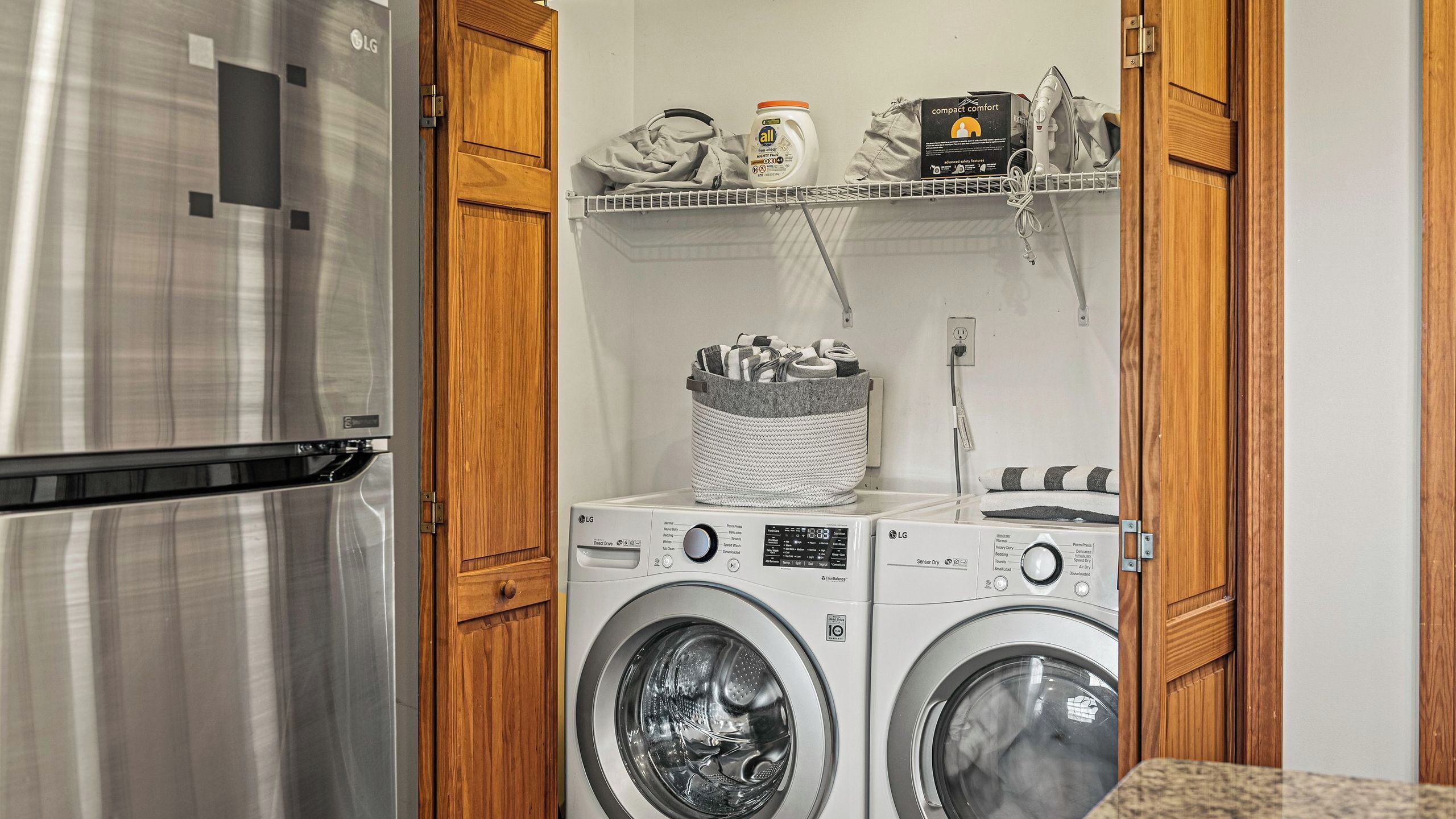 A compact laundry area with a washing machine, dryer, and a shelf with laundry supplies.