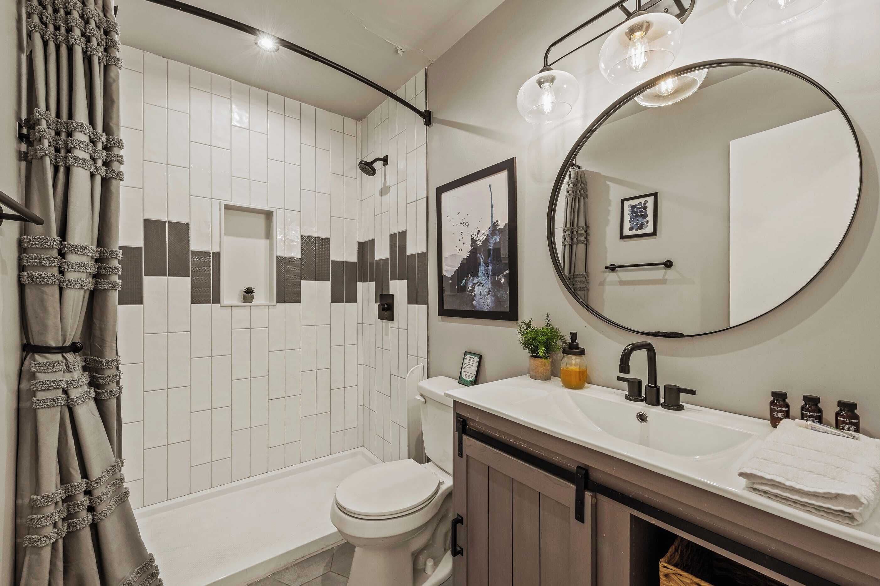 A modern bathroom with a white tiled shower, a toilet, a sink with a mirror, and a towel rack.