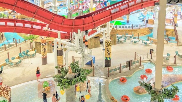 An indoor water park with a red water slide, multiple pools, and seating areas.