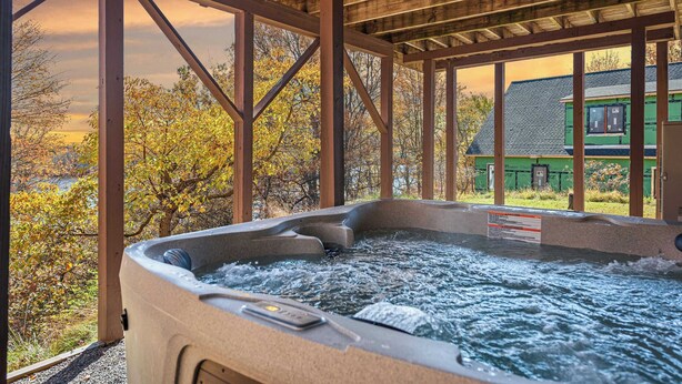Un bain à remous avec une structure en bois, offrant une vue sur les arbres et une maison en arrière-plan.