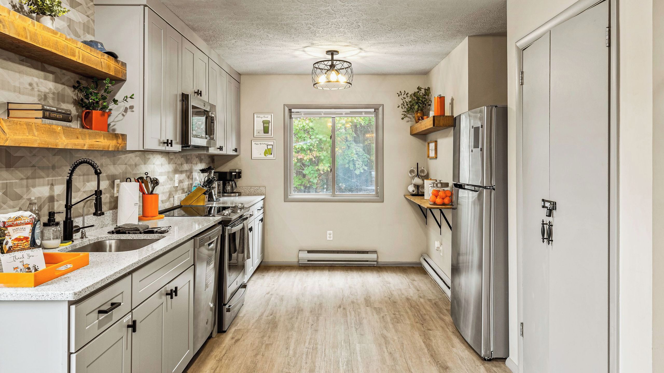 Una cocina con un refrigerador de acero inoxidable, una ventana y un horno empotrado.