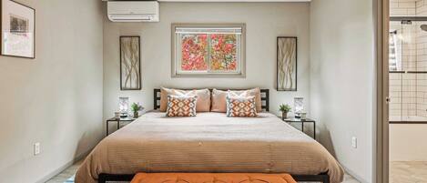 A bedroom with a large bed, a bench, a window with a view, and a door leading to a bathroom.