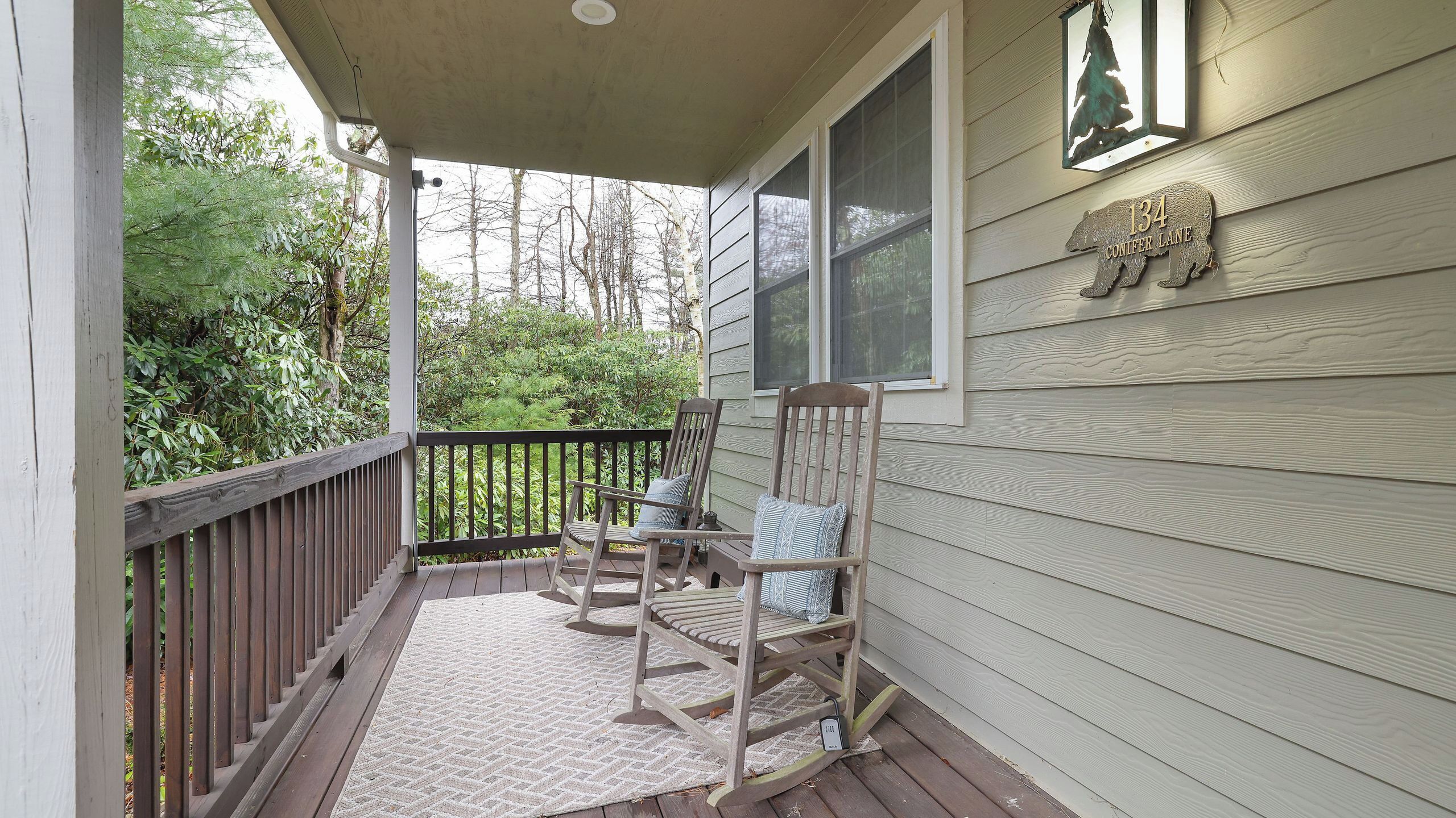 A porch with two rocking chairs, a wooden railing, and a house number sign.