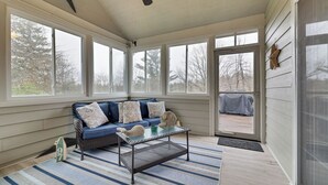 A sunroom with a blue sofa, a glass coffee table, and a view of the outdoors. - The Nest at Pinecrest by Avantstay Spacious Deck, Game Room, Fire Pit (Pocono Pines)