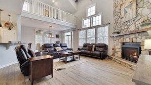 A spacious living room with leather sofas, a fireplace, and a stone wall. - The Nest at Pinecrest by Avantstay Spacious Deck, Game Room, Fire Pit (Pocono Pines)