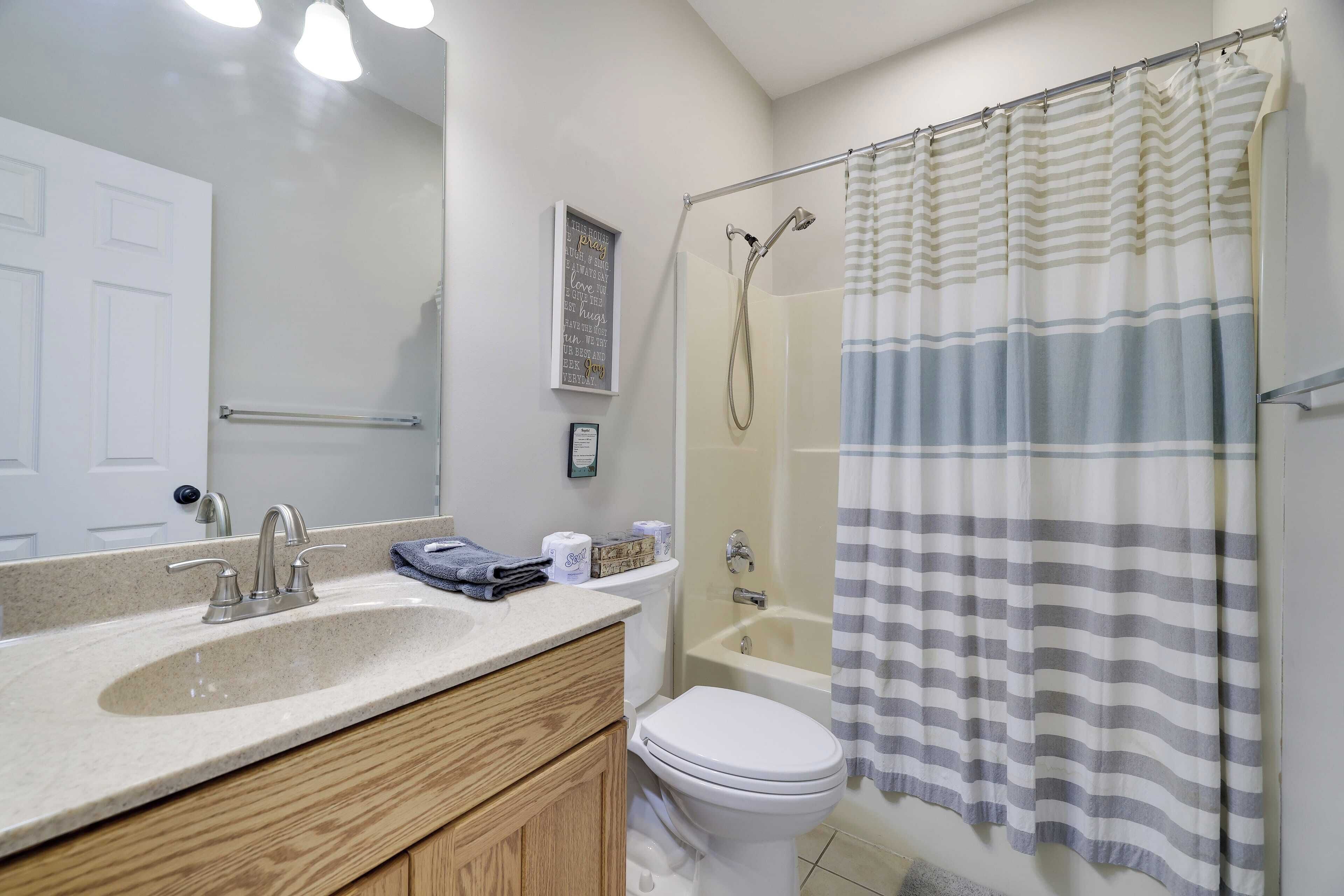 A bathroom with a sink, mirror, toilet, shower, and a striped shower curtain.