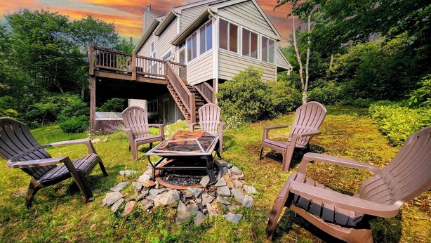 A house with a deck, outdoor seating with Adirondack chairs, and a fire pit. - The Nest at Pinecrest by Avantstay Spacious Deck, Game Room, Fire Pit (Pocono Pines)