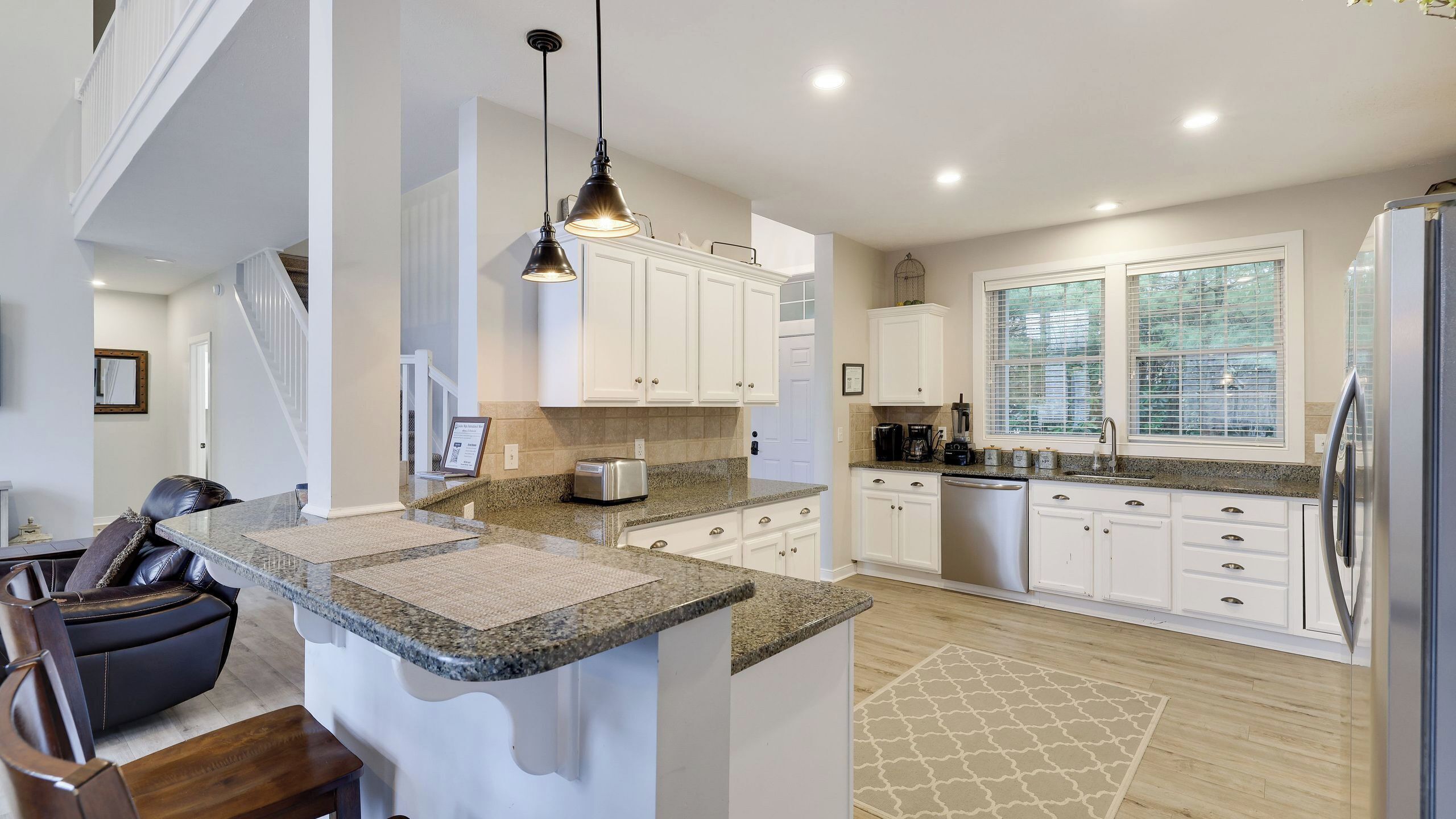 A modern kitchen with white cabinets, granite countertops, a built-in dishwasher, and a large window.