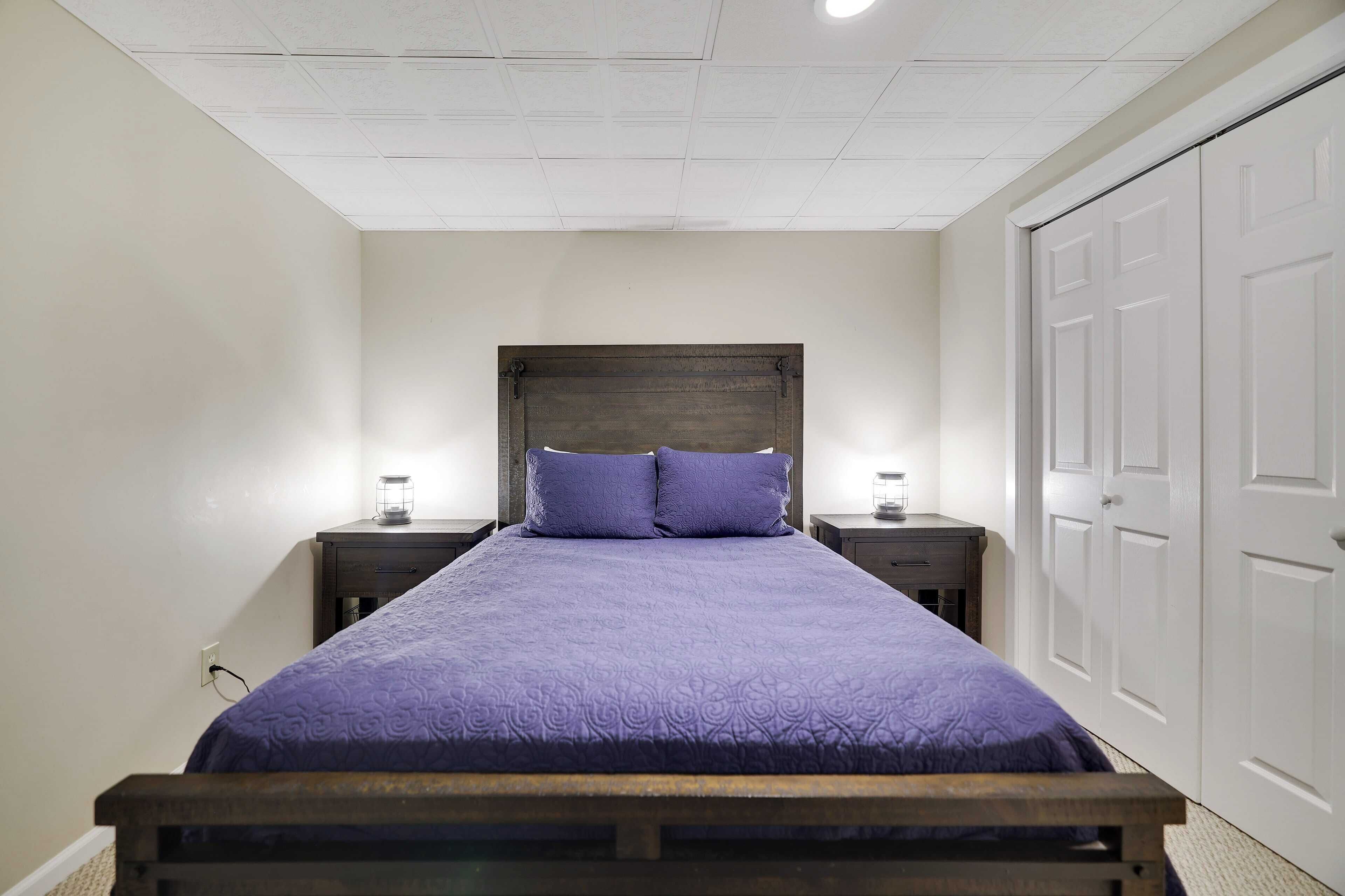 Une chambre à coucher avec un lit en bois, une literie violette, deux tables de chevet avec des lampes et une porte blanche.