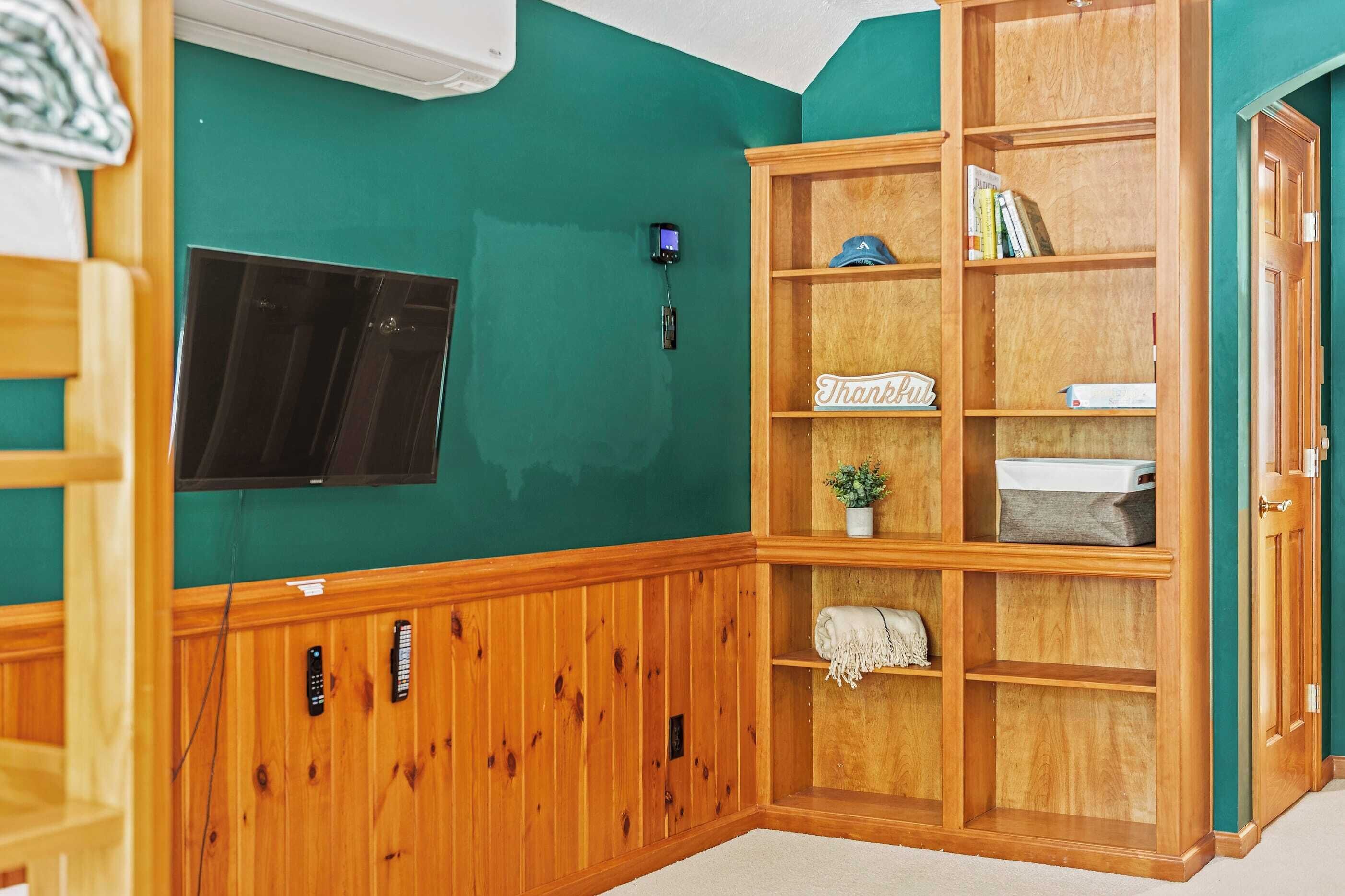 Une pièce aux murs de couleur turquoise, un meuble en bois avec des étagères, un téléviseur à écran plat fixé au mur et un thermostat également fixé au mur.