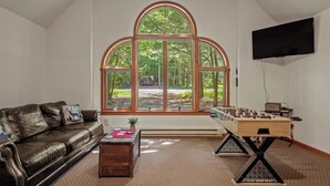 Ein Wohnzimmer mit einer Ledersofa, einem Kicker, einem großen Bogenfenster und einem Flachbildfernseher.