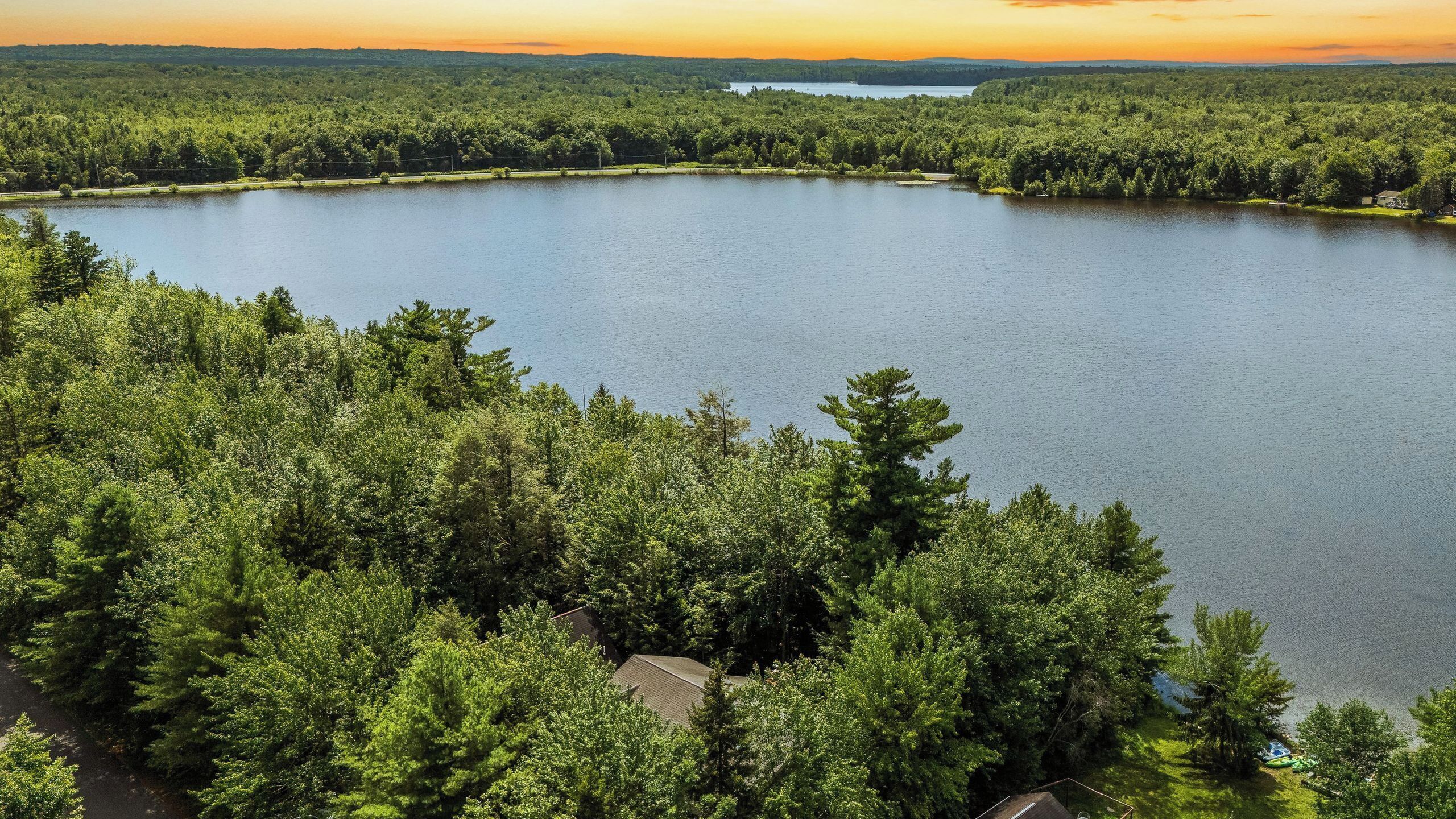 A lake surrounded by dense forest, with a small house near the water's edge.