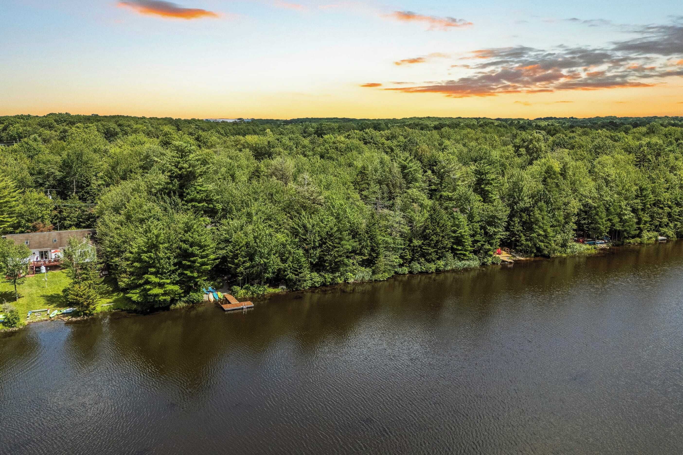 A lakeside property with dense forest, a dock, and a house with a deck.