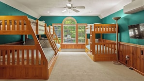 A bunk room with wooden bunk beds, a ceiling fan, a large arched window, and a television. - Tranquil Waterside by Avantstay Lakefront + Dock, Game Room, Views (Pocono Summit)