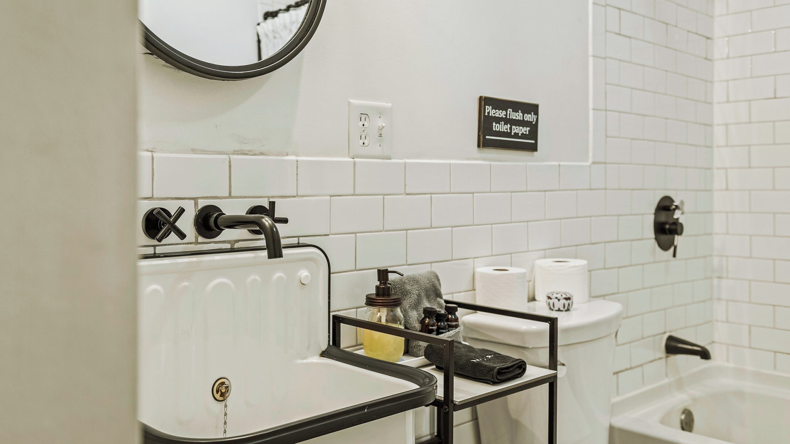 A bathroom with a white sink, a toilet, and a bathtub. There is a sign on the wall that says "Please flush only toilet paper."