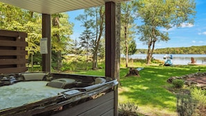 Un bain à remous avec une terrasse en bois, un panneau indiquant les règles de sécurité et une vue sur un lac bordé d’arbres et doté d’un quai.