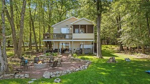 A two-story cabin with a deck, surrounded by trees. - Lake Daze by Avantstay Lakefront w/ Modern Interior, Enclosed Porch & Hot Tub (Pocono Summit)