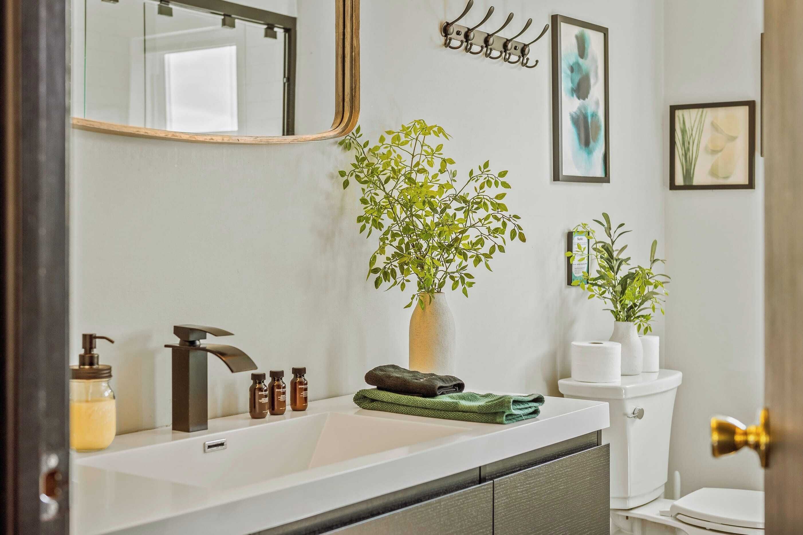 A bathroom with a white sink, a mirror, a plant, and a toilet.