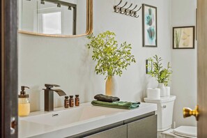A bathroom with a white sink, a mirror, a plant, and a toilet. - Mountain Mindset by Avantstay Pool, Hot Tub, Game Room, Firepit (Long Pond)