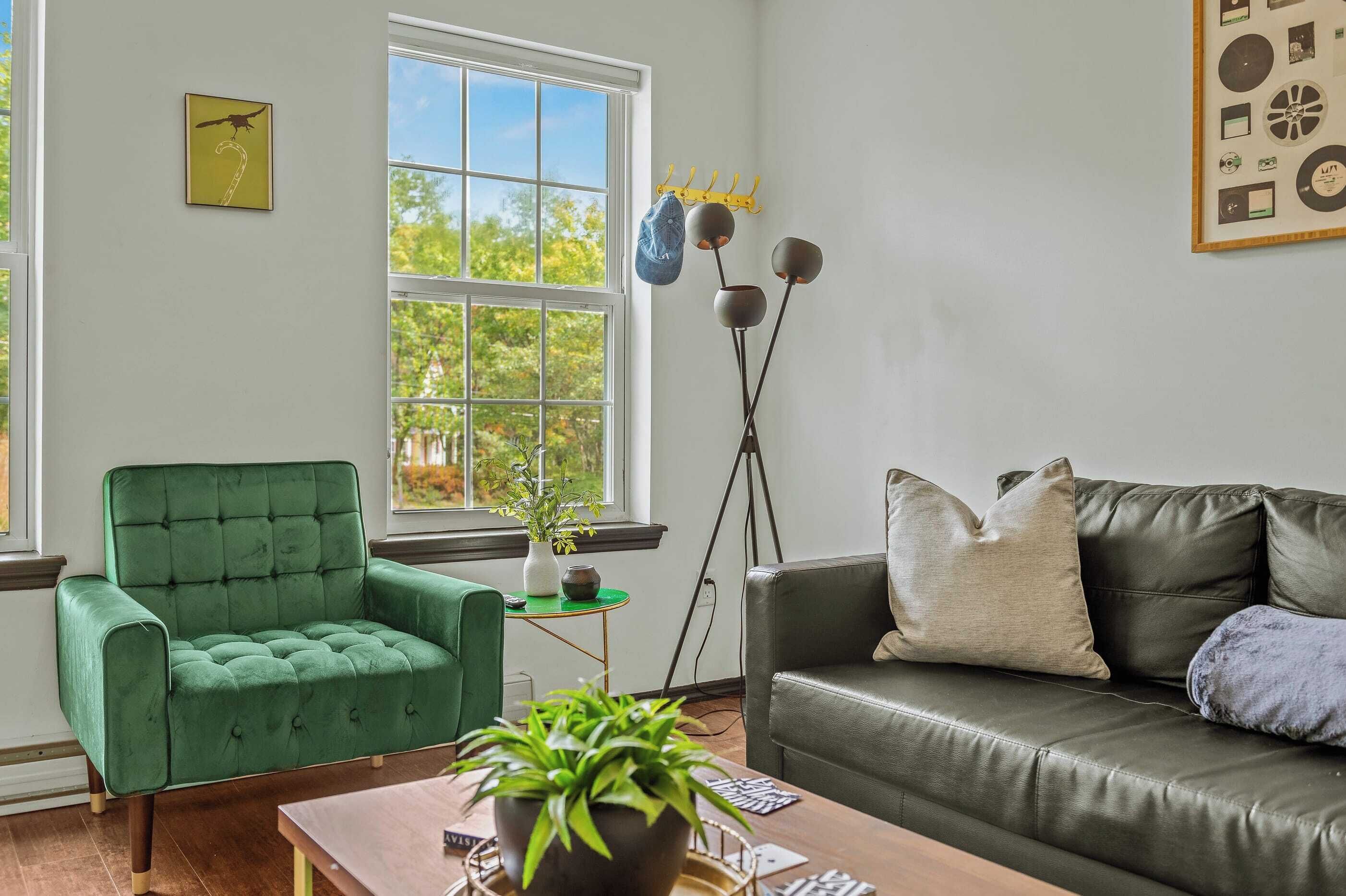 A living room with a green armchair, a leather sofa, a coffee table, and a window with a view of trees.