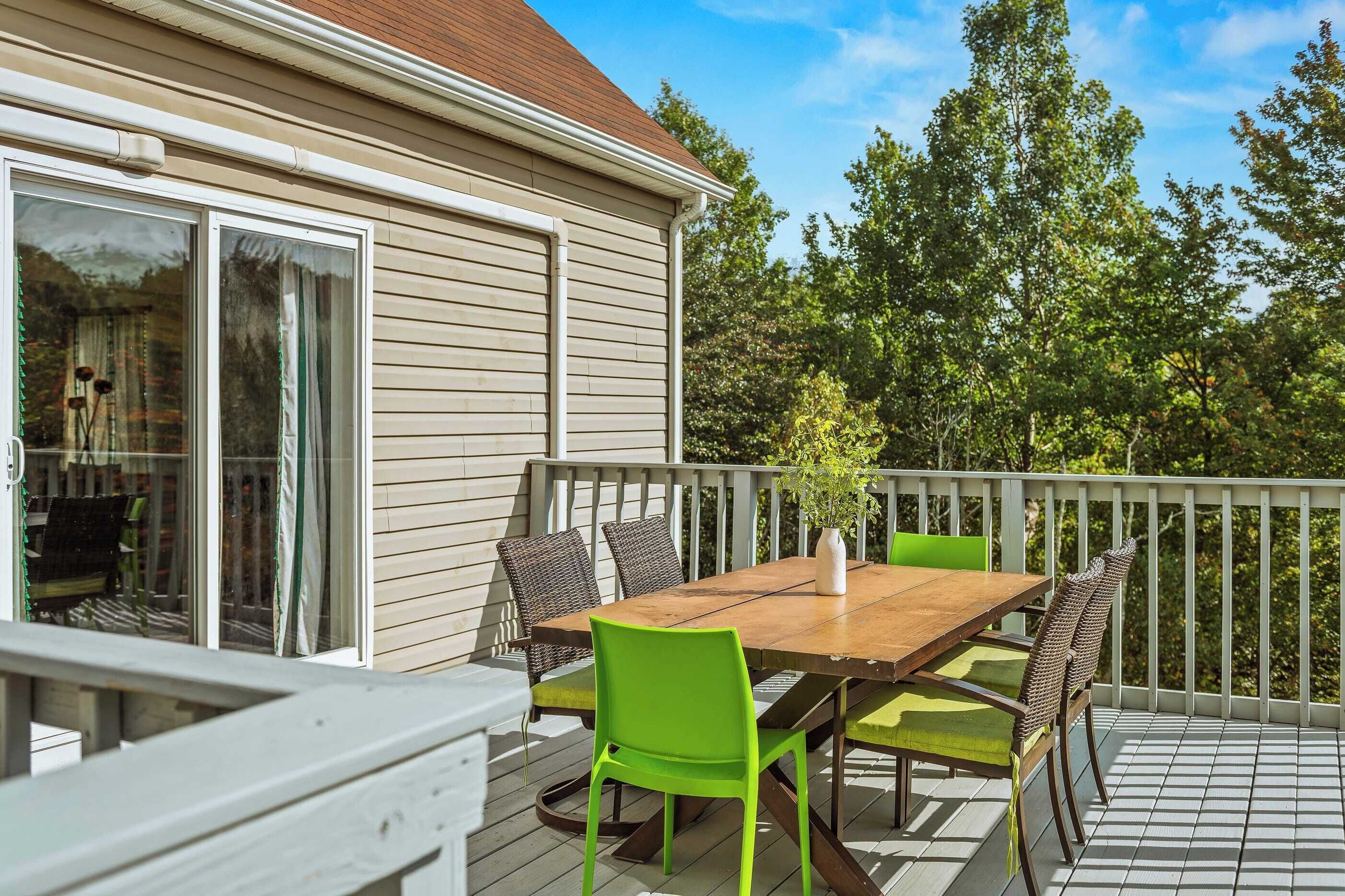 Een terras met een houten tafel en stoelen, een bloempot en uitzicht op bomen.