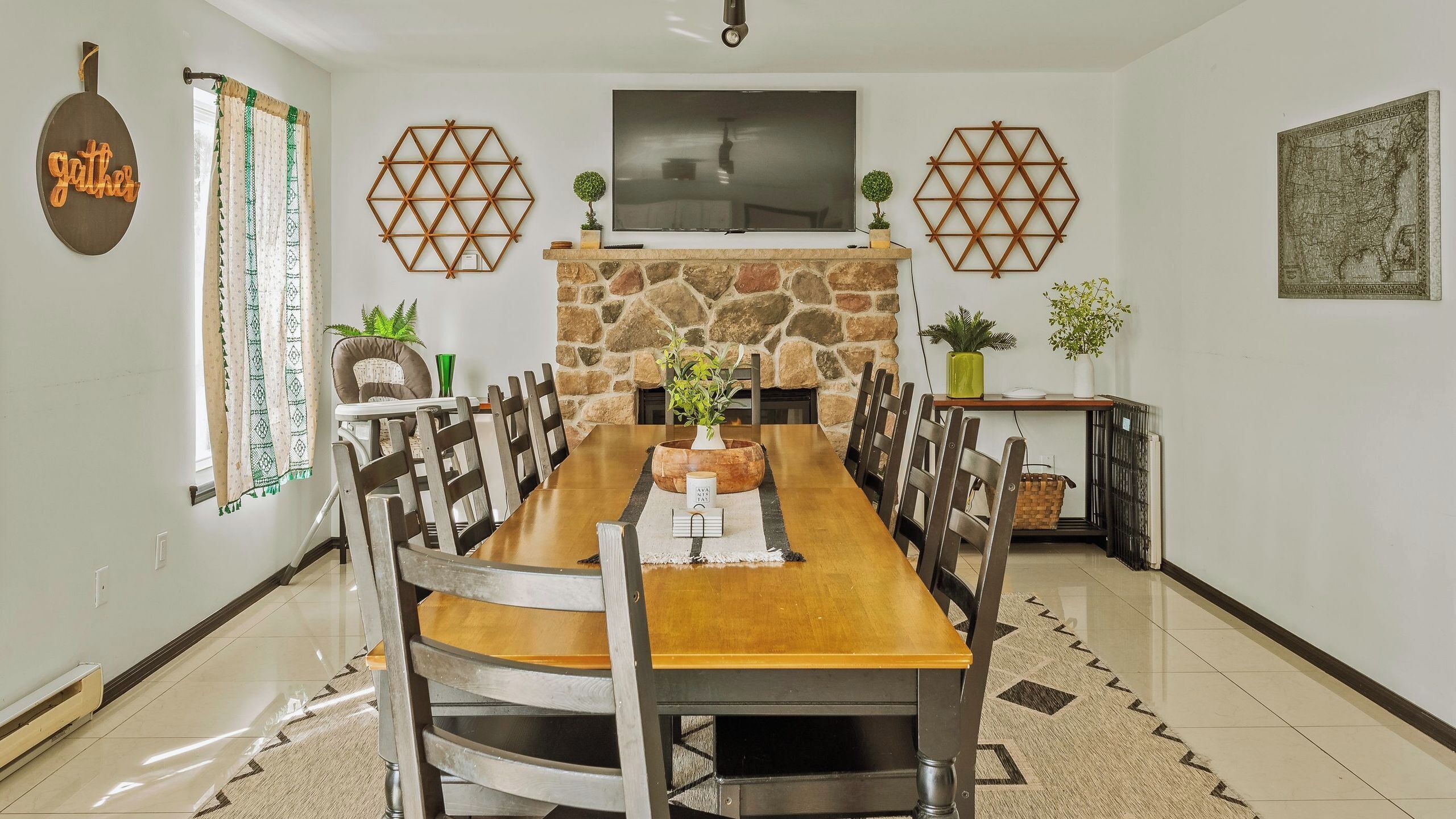 A dining area with a stone fireplace, a flat-screen TV, and hexagonal wall decorations.