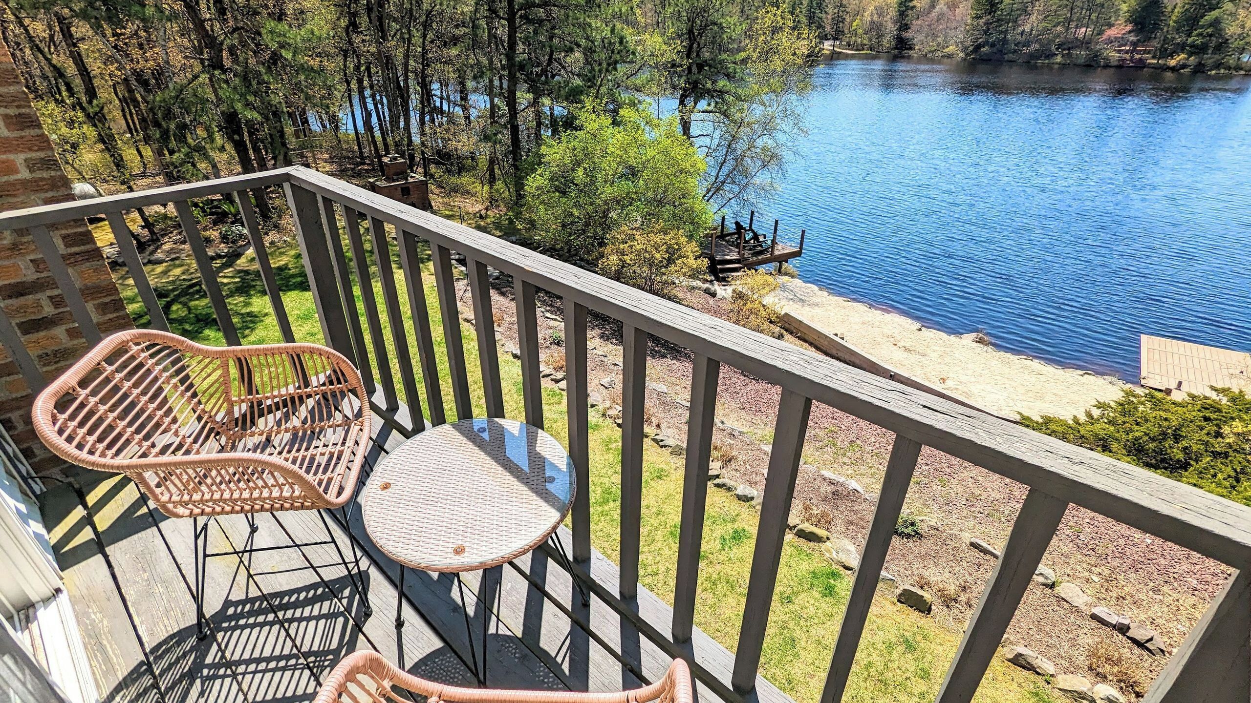 A balcony with wicker chairs, a small round table, and a view of a lake surrounded by trees.