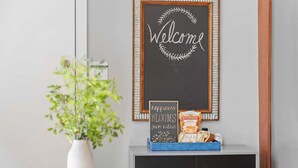 Una habitación con un cartel de bienvenida, una planta pequeña y una bandeja con pan y un frasco de mermelada.
