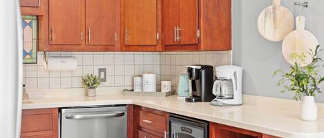 A kitchen with wooden cabinets, a countertop, a coffee maker, a dishwasher, and a potted plant.