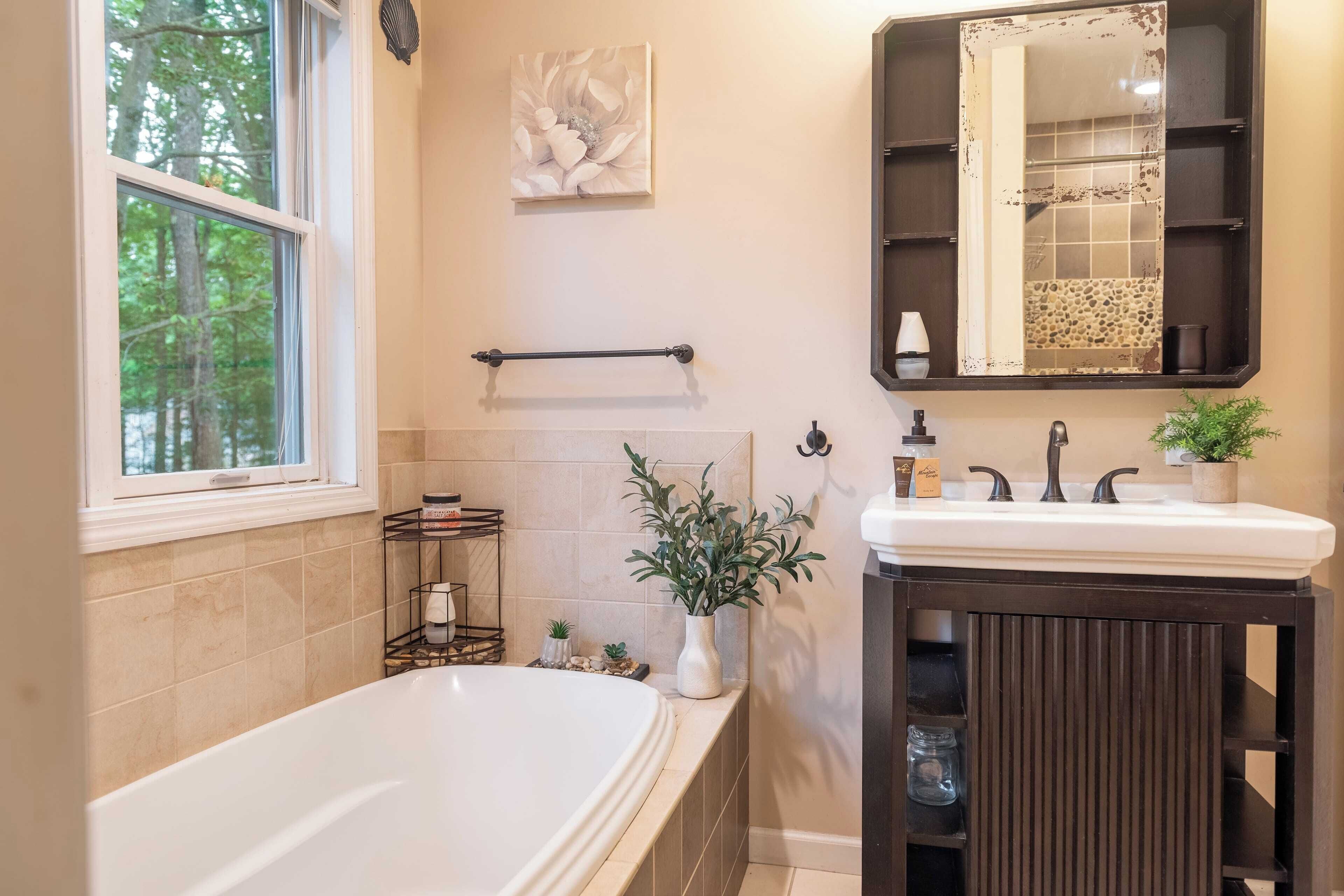 A bathroom with a bathtub, a sink, a mirror, and a window.