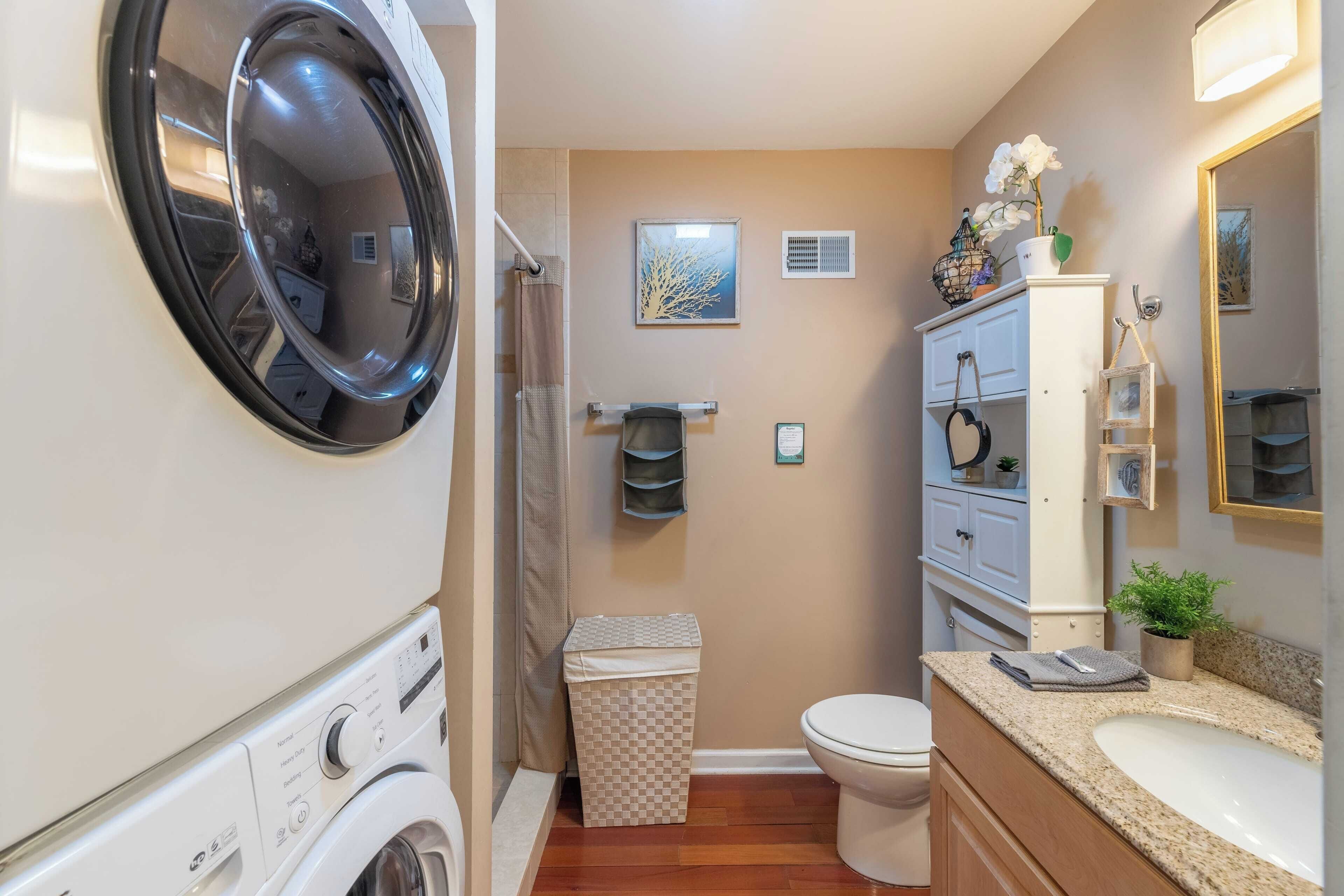 A compact bathroom with a washing machine, toilet, sink, and a small trash bin.