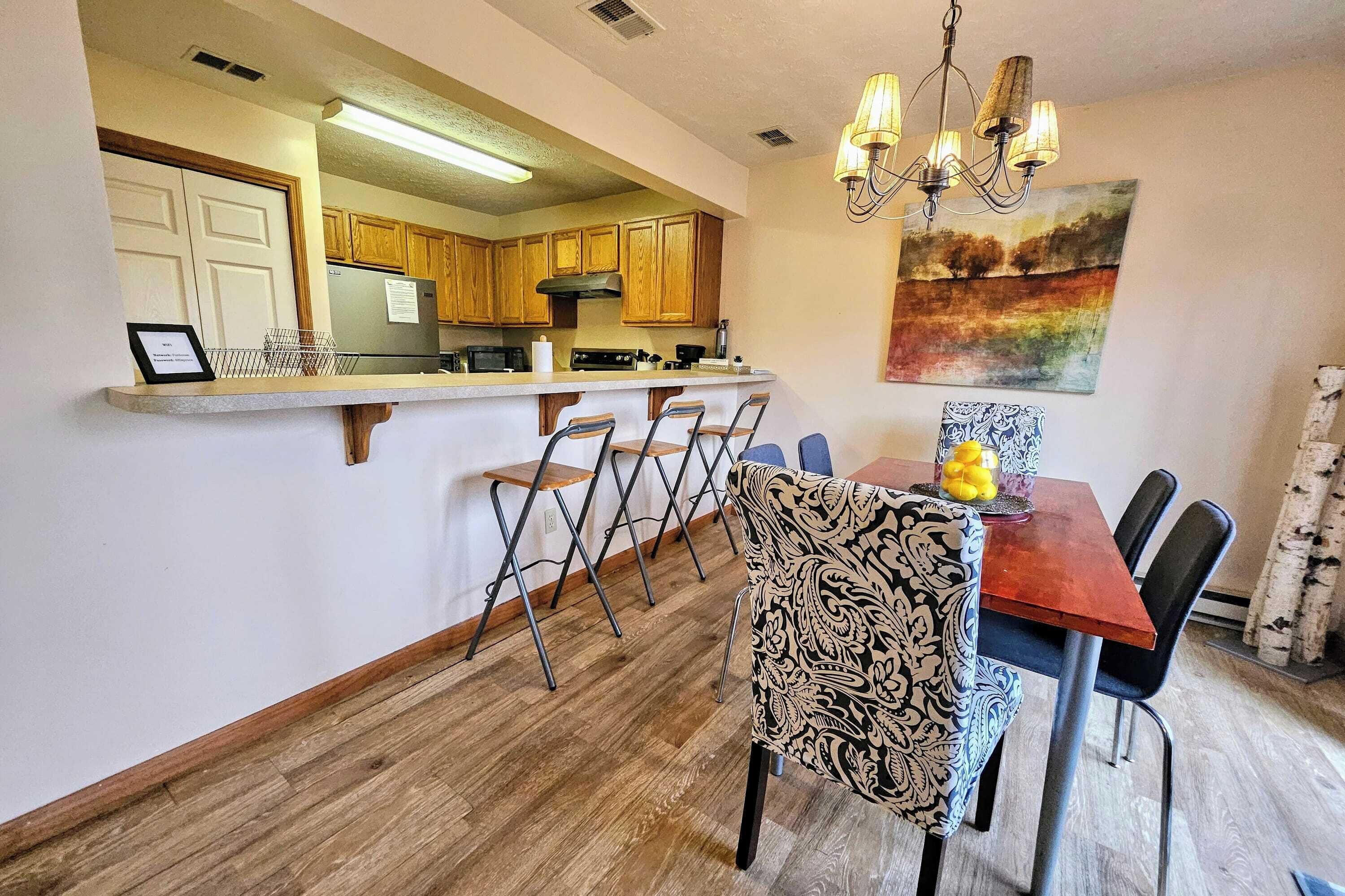A kitchen with wooden cabinets, a stainless steel refrigerator, and a bar area with bar stools.