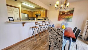A kitchen with wooden cabinets, a stainless steel refrigerator, and a bar area with bar stools. - Summit Serenity by Avantstay Central Location w/ Mountain Views & Deck (Tannersville)