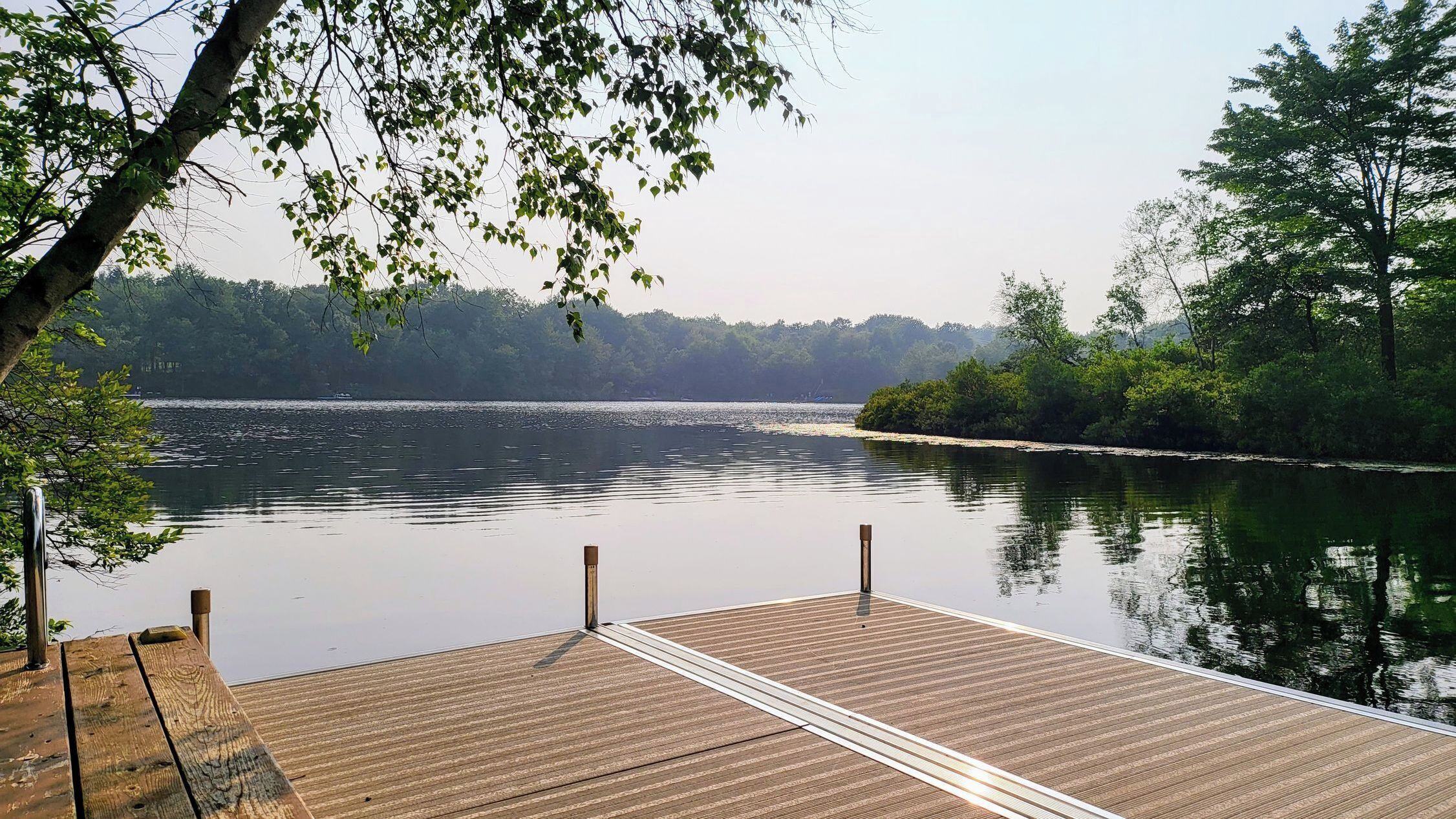 A wooden dock extending into calm water with a forested shoreline in the background.