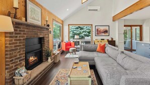 A living room with a brick fireplace, a grey sofa, and a wooden ceiling. - Waterside Haven by Avantstay Lakefront, Hot Tub, Game Room, Fire Pit (Long Pond)