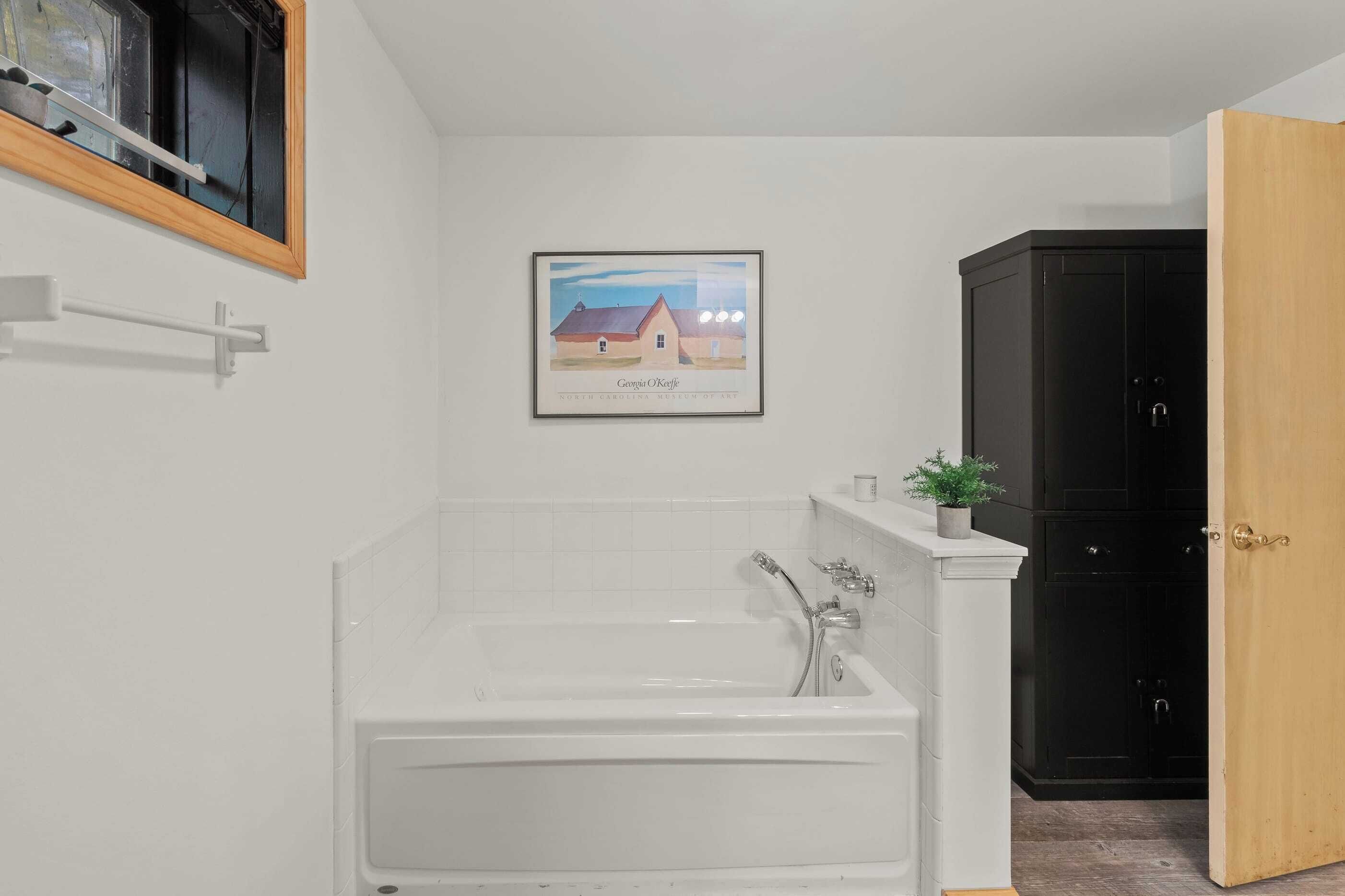 Een badkamer met een witte badkuip, een inlijsting schilderij aan de muur, en een zwart kastje.