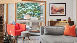 A living room with a fireplace, a sofa, a red chair, a side table, and a bookshelf. - Waterside Haven by Avantstay Lakefront, Hot Tub, Game Room, Fire Pit (Long Pond)